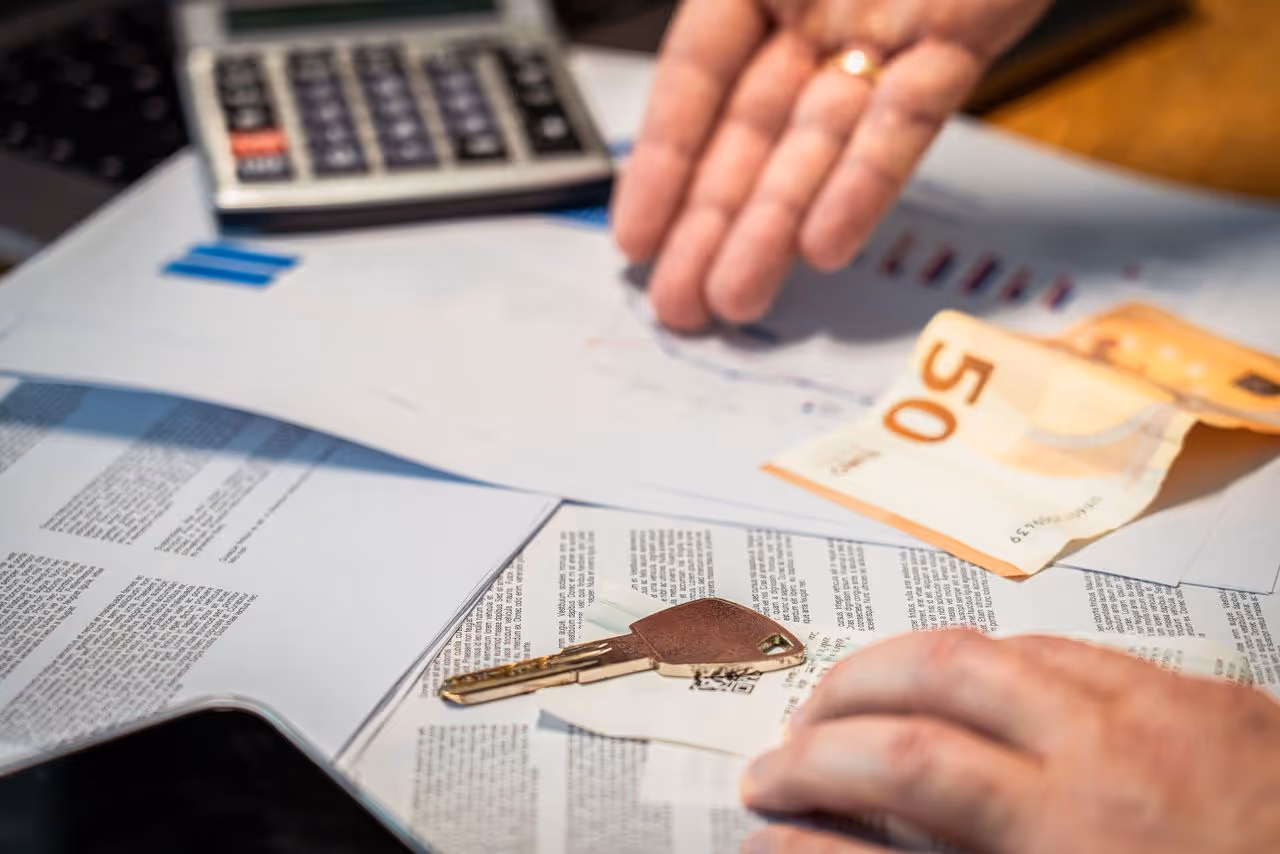 Una calculadora, documents, un bitllet de 50 euros i una clau sobre una taula.
